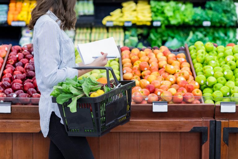 On voit ici une jeune femme dans un supermarché devant la section des légumes.