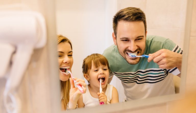 On voit ici une petite famille, maman, papa et fillette se brosser les dents pour une meilleure santé bucale.