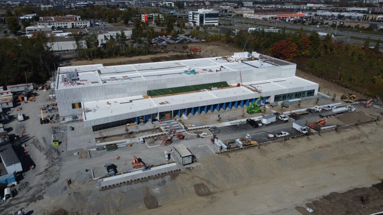 Mis en chantier au coût de 180 M$ en novembre 2022, le centre de production de Moderna Canada est situé au nord-est des boulevards Notre-Dame et Armand-Frappier au cœur même de la Cité de la Biotech.