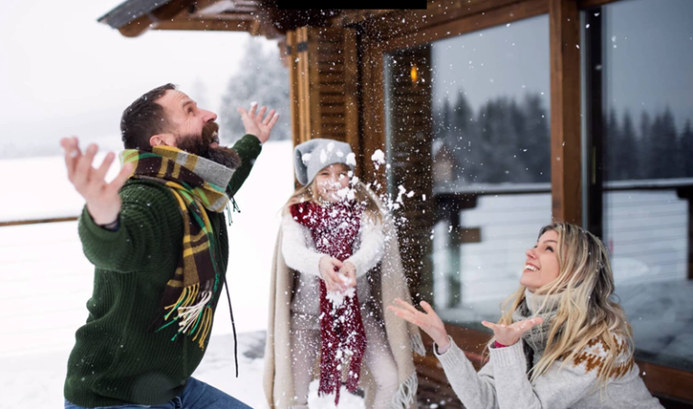 Un couple et leur fille s’amusent avec la neige sur le balcon du chalet qu’ils louent.